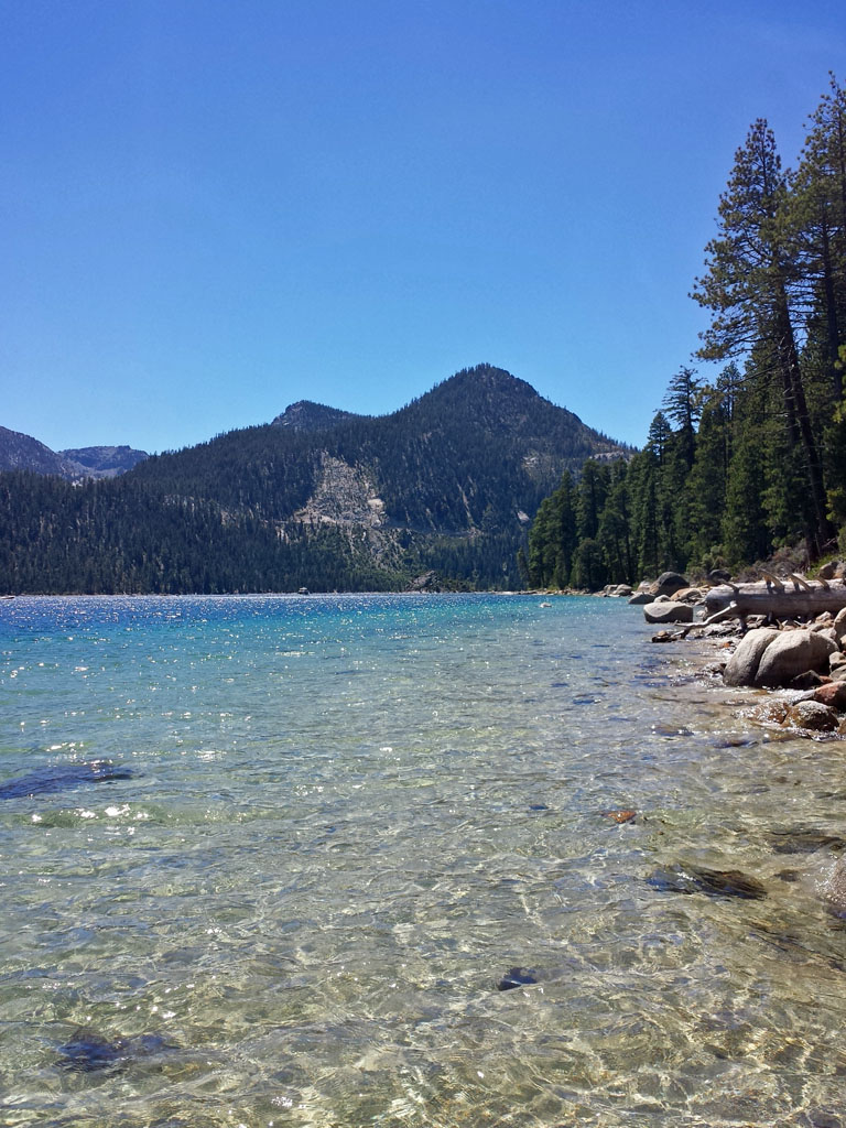 a clear lake with rocks and trees on the shore