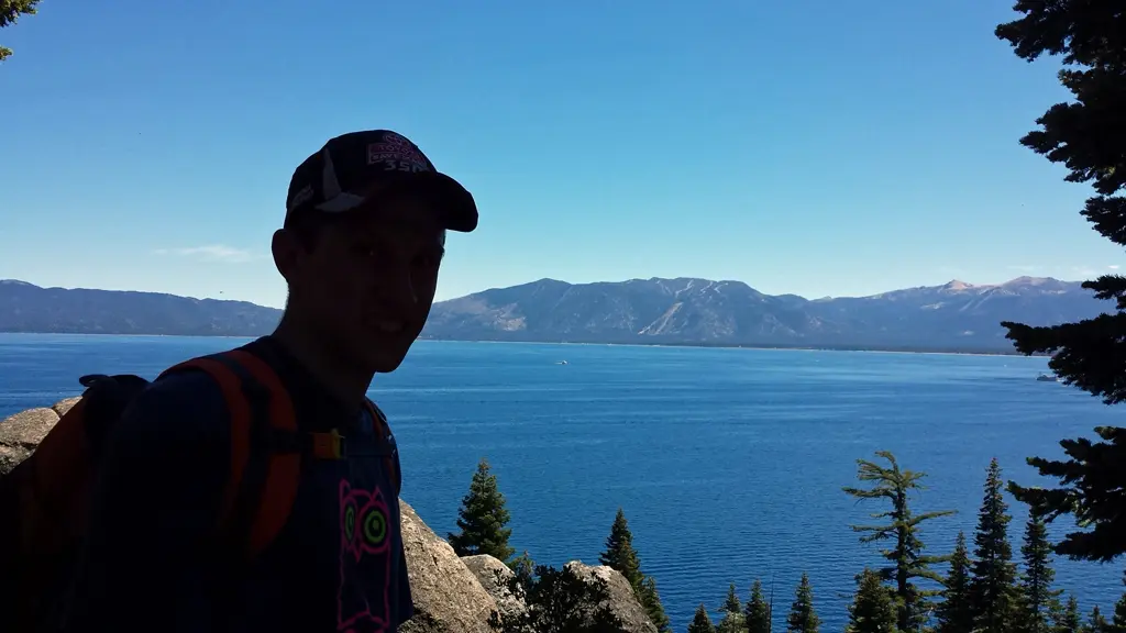 a man with a backpack and hat standing on a mountain overlooking a lake