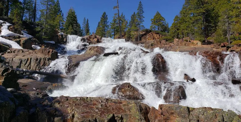 a waterfall in the mountains with trees and rocks