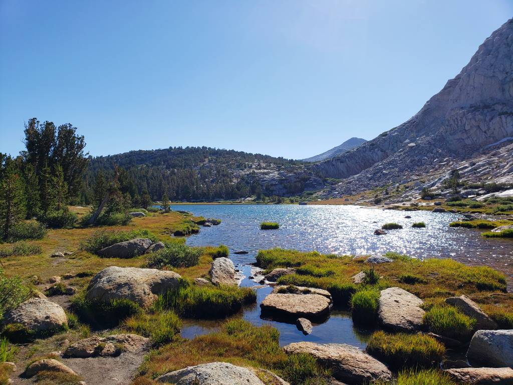 a lake surrounded by rocks and grass in the mountains