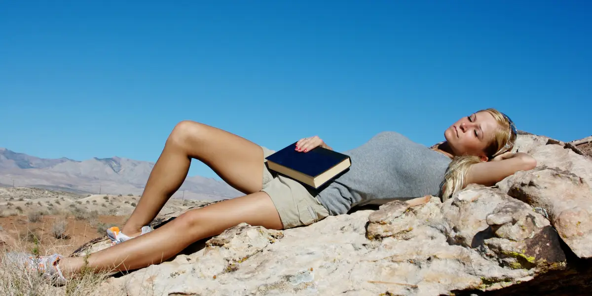 Girl Laying on Rock in sun napping with book in hand