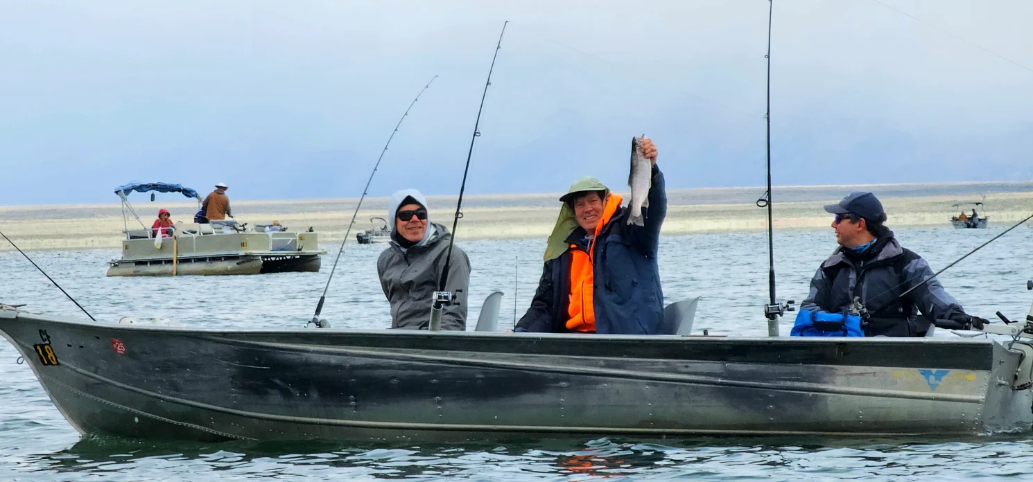 Man in hoodie holds up trout on crowley lake in boat