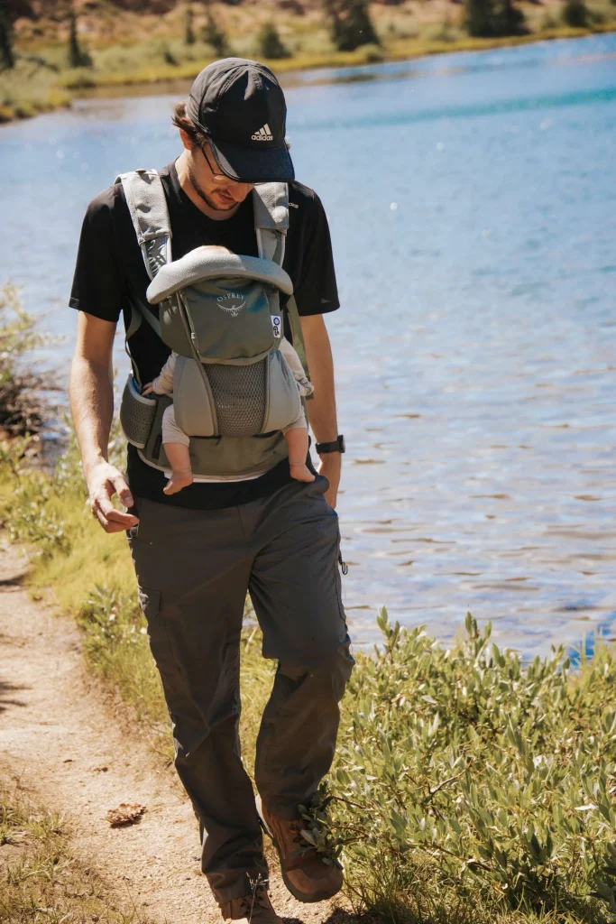 Young man hiking near lake with child in osprey poco soft carrier