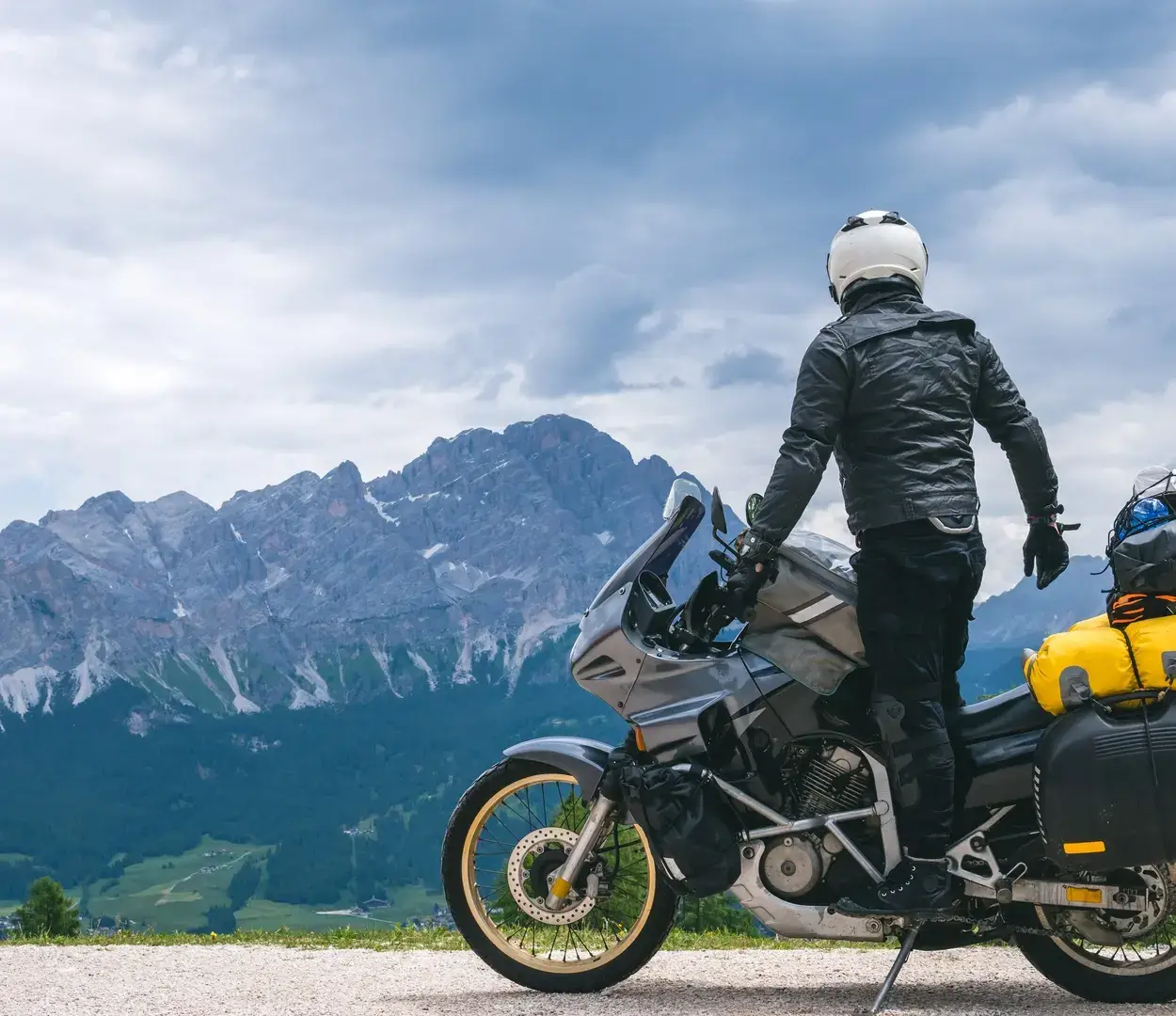 A motorcycle rider in full gear standing up on their motorcycle while looking at a mountain range in the distance.